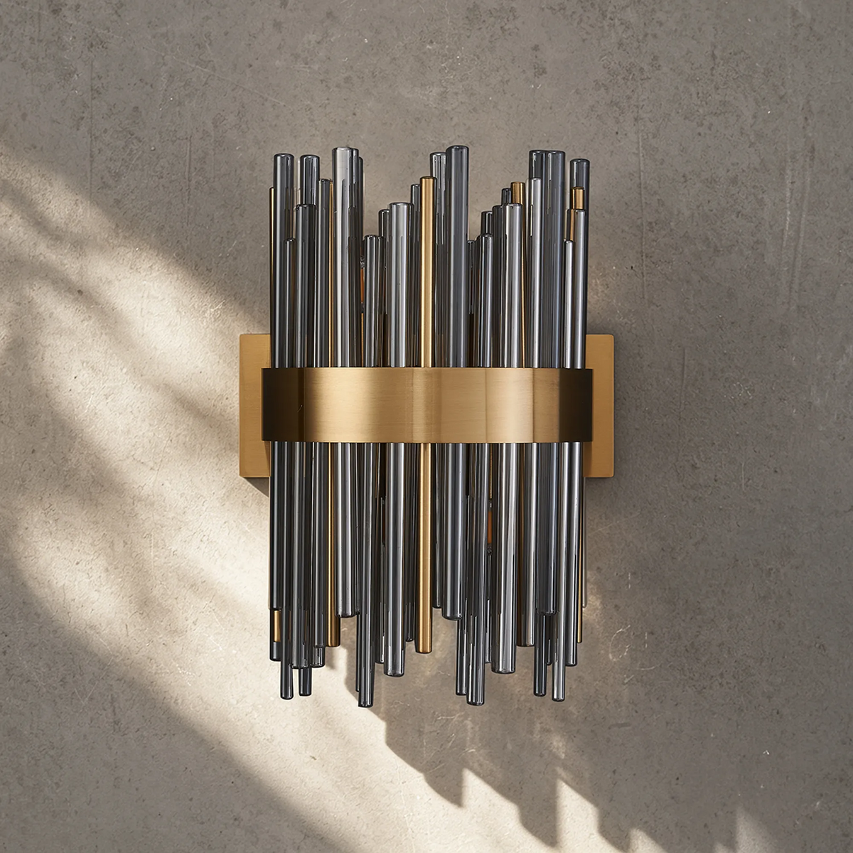 Wall sconce with vertical glass rods in various lengths and a horizontal brass band