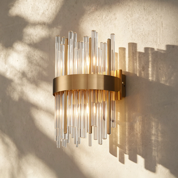 Brass and glass tube wall sconce with warm light on a textured wall