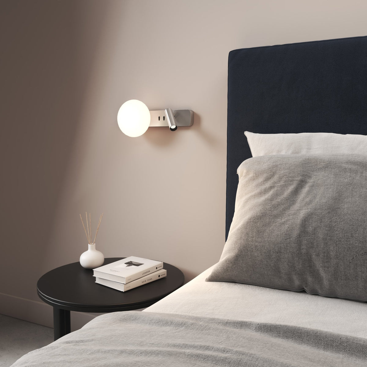 Bedroom with a wall-mounted light fixture, a dark blue headboard, and a black side table with books