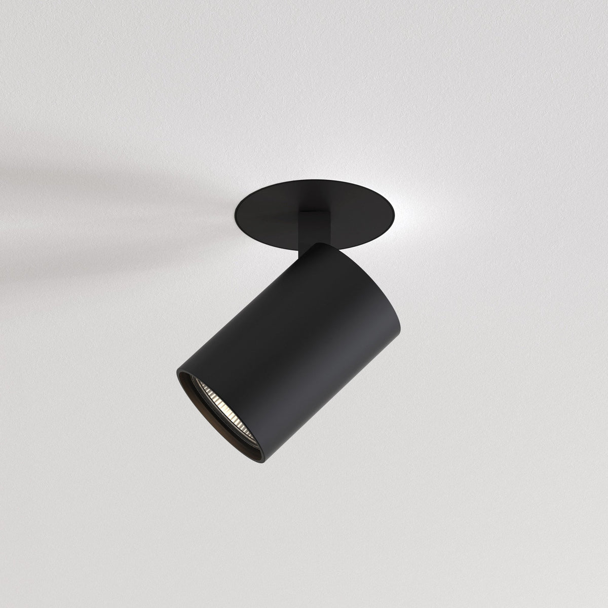 Black cylindrical ceiling spotlight with a circular base, angled downwards, against a white ceiling