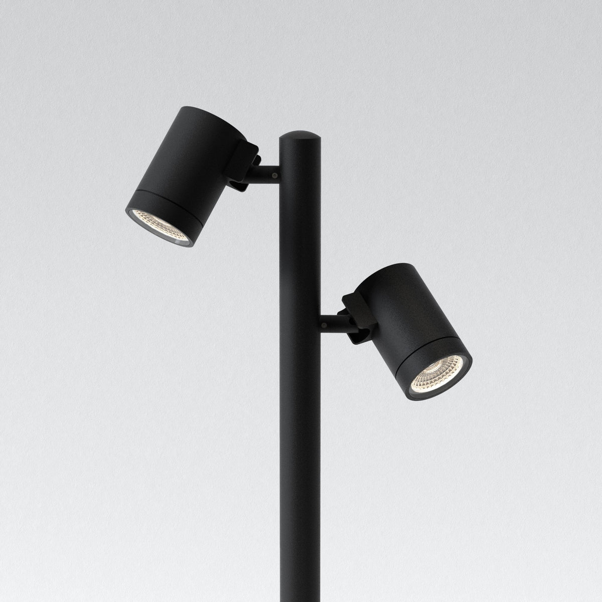 Two black cylindrical spotlights attached to a black pole, angled downwards with illuminated LED bulbs