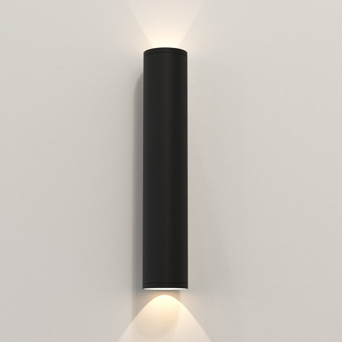Black cylindrical wall light with light shining upwards and downwards on a white wall