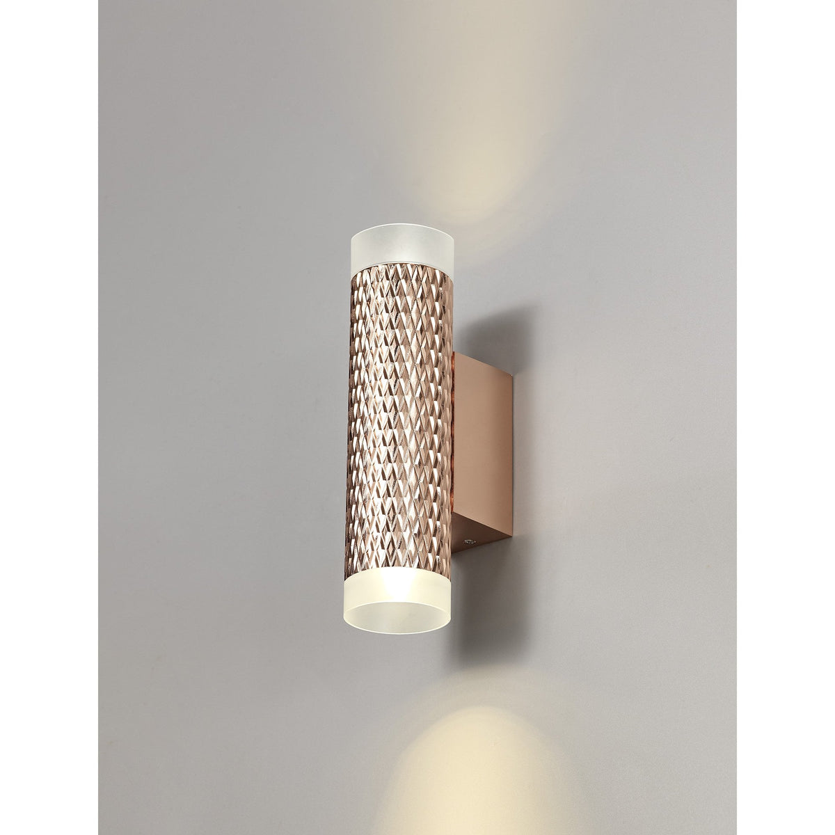 A rose gold textured wall light casts light upwards and downwards on a grey wall.