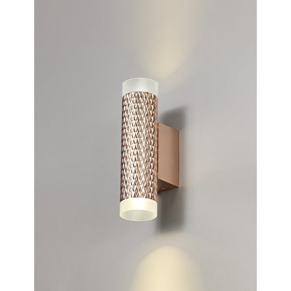A rose gold textured wall light casts light upwards and downwards on a grey wall.