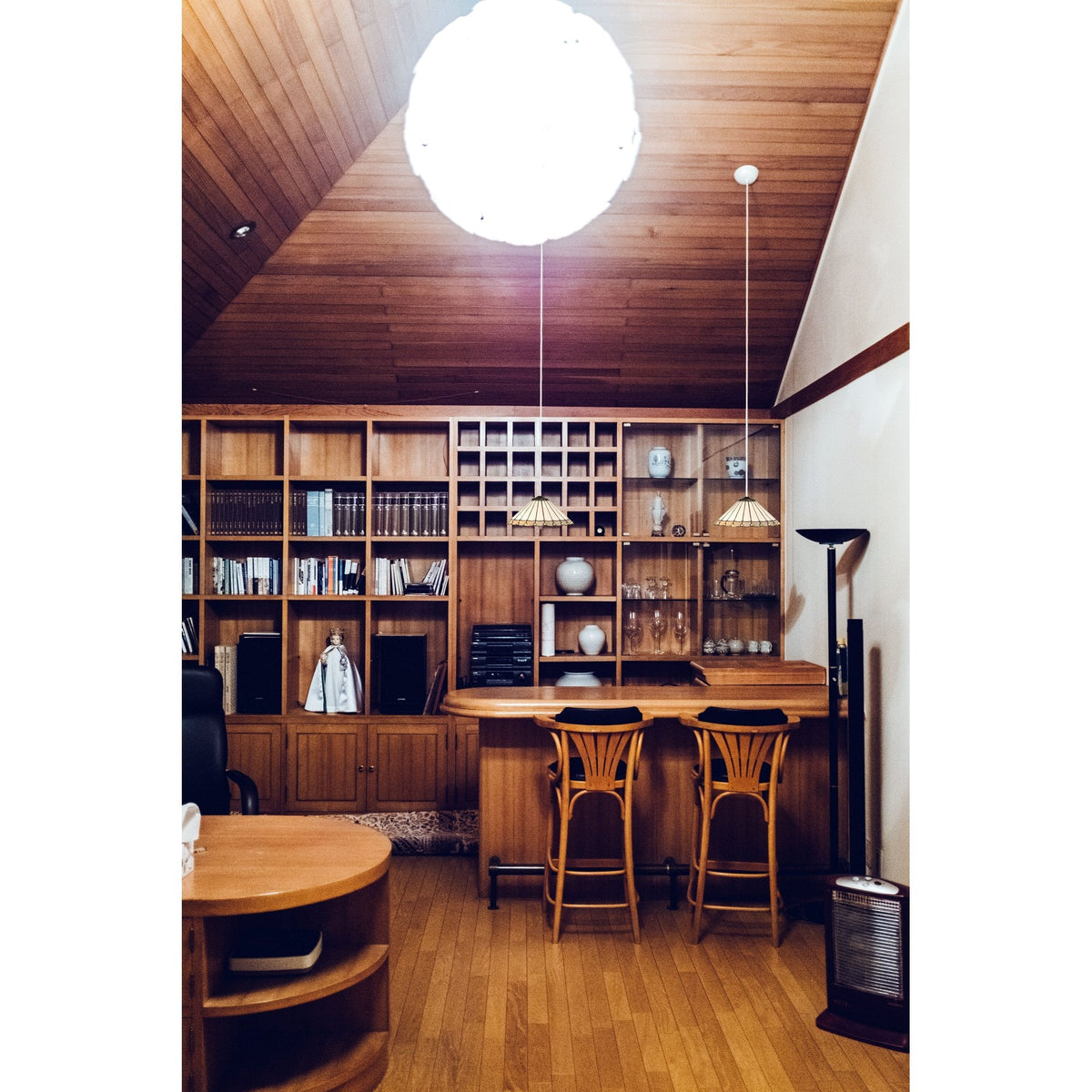 A home bar area with wooden panelled walls, a large bookshelf, and a round light fixture.