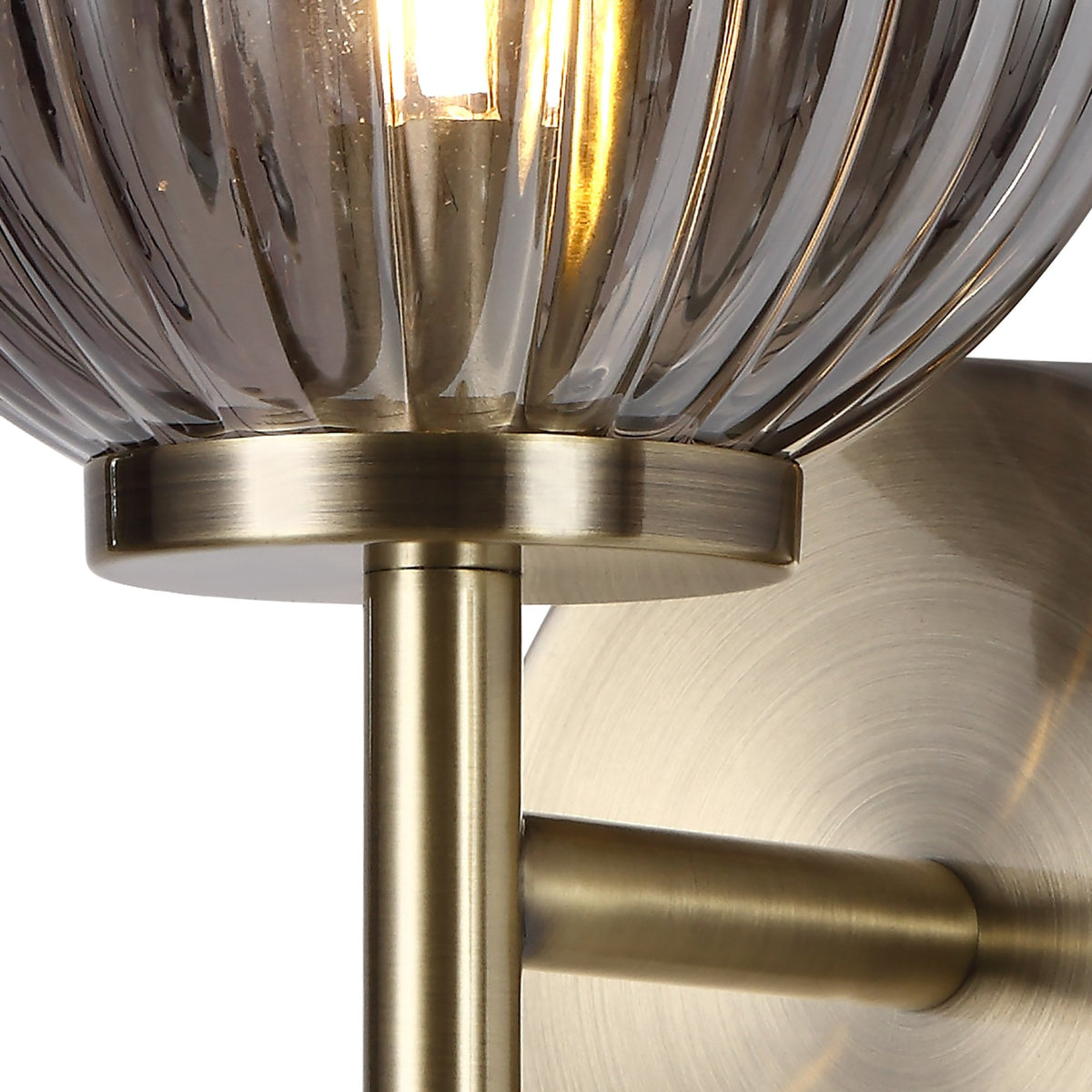 Close-up of the antique brass fitting and ribbed smoked glass of the wall light.
