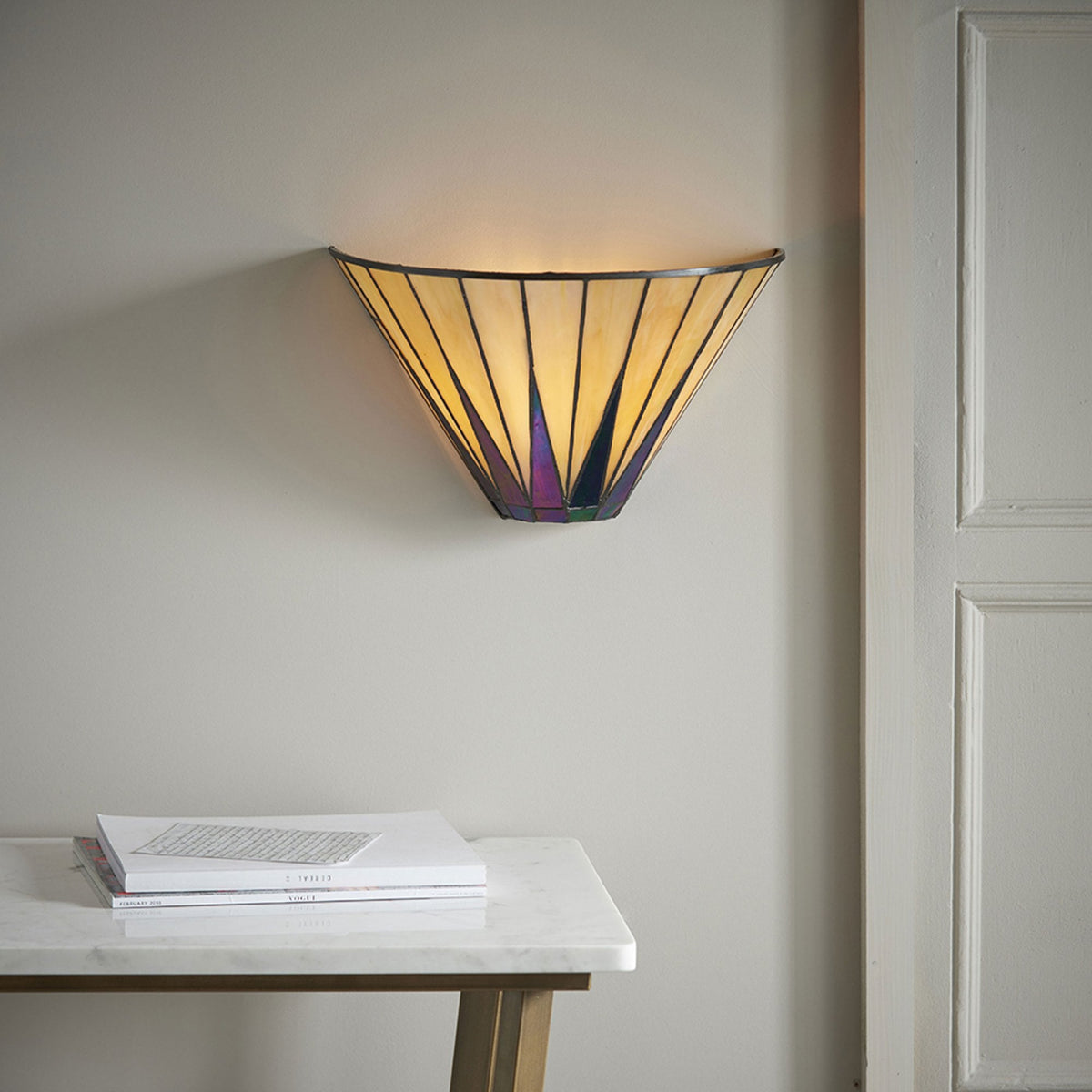 A wall light with a yellowish stained glass shade and purple accents illuminates a room.
