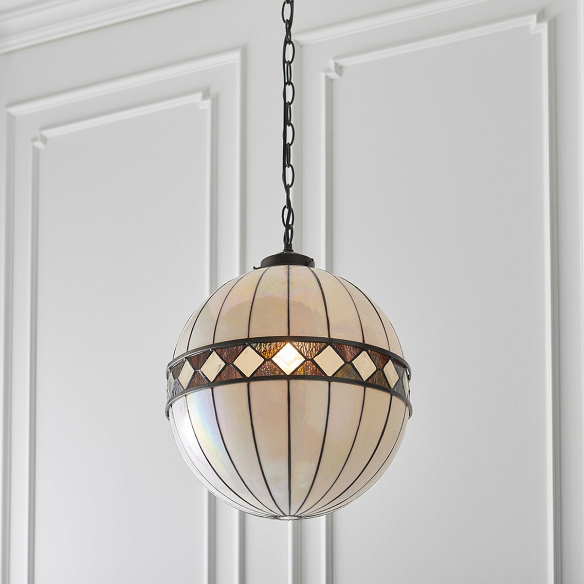 A close-up of a white and brown stained glass globe pendant light hanging from a ceiling.