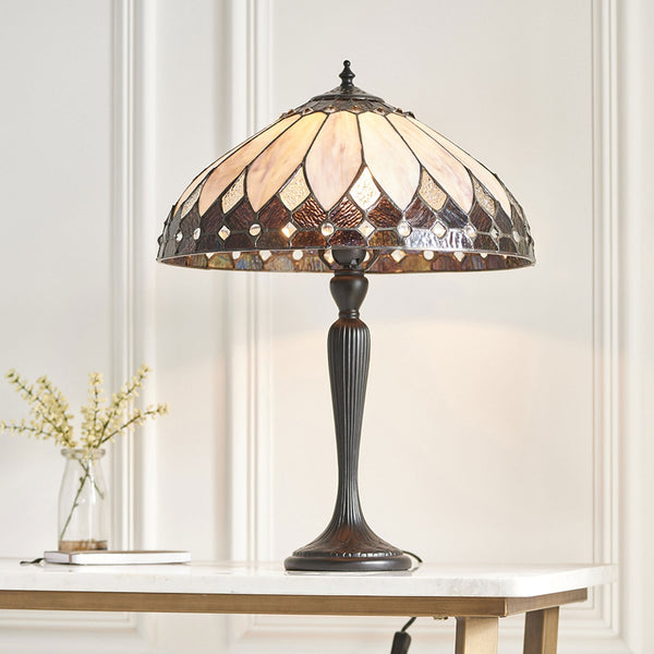 An ornate table lamp on a white marble table with a vase of flowers.