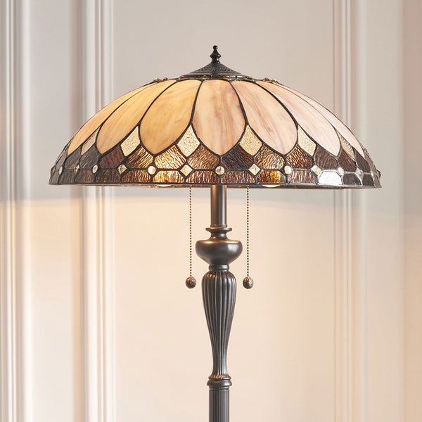 Close-up of a Tiffany-style floor lamp with an intricate amber and cream stained-glass shade.