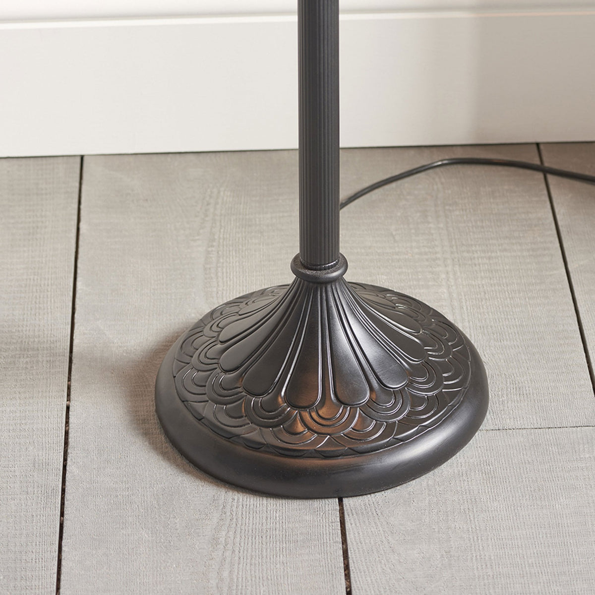 Close-up of the ornate, dark bronze base of a Tiffany-style floor lamp on a wooden floor.