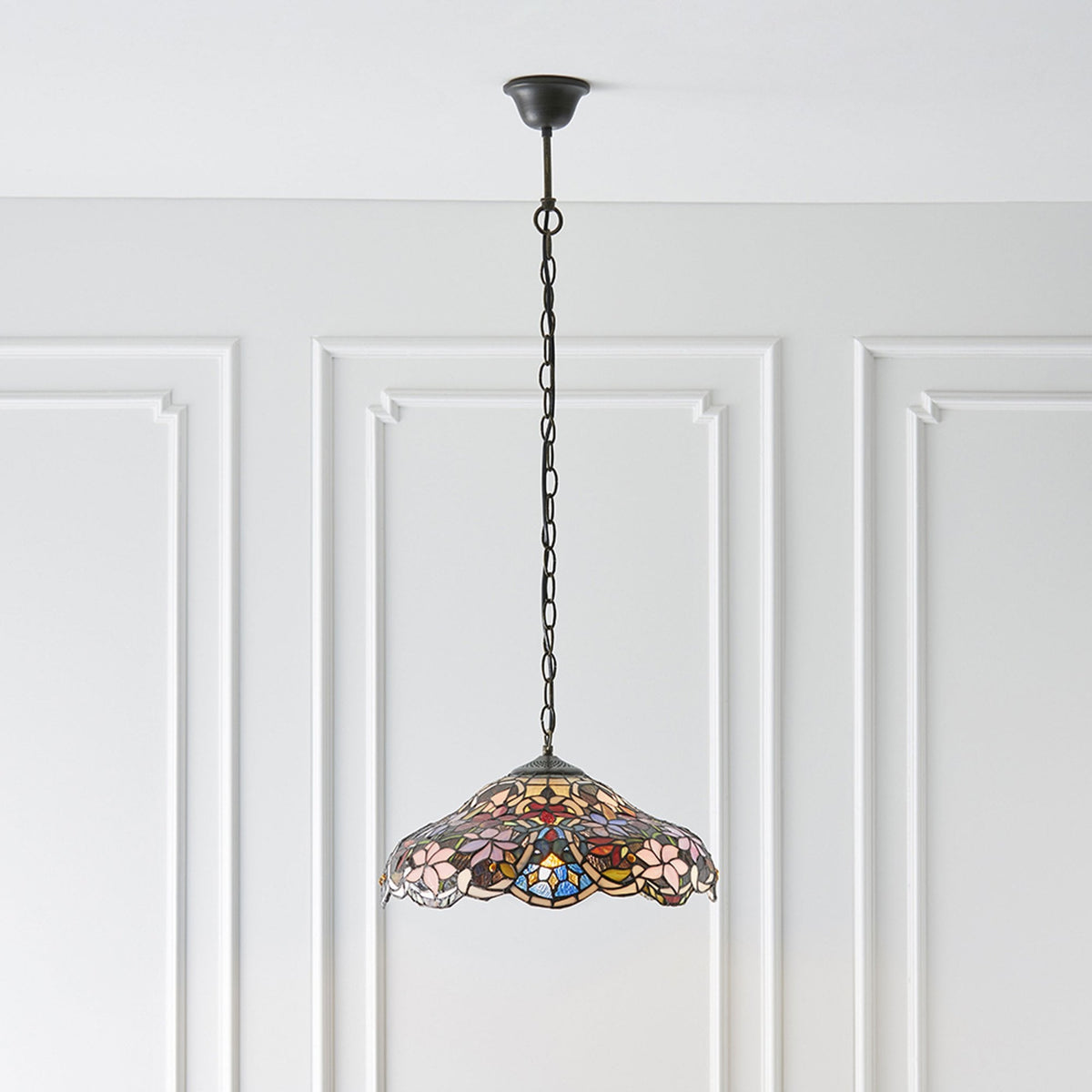 A Tiffany-style pendant light with a floral stained-glass shade hanging in a room.