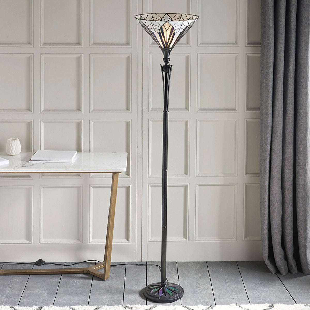 A decorative floor lamp with a geometric stained-glass shade in a room. A period.