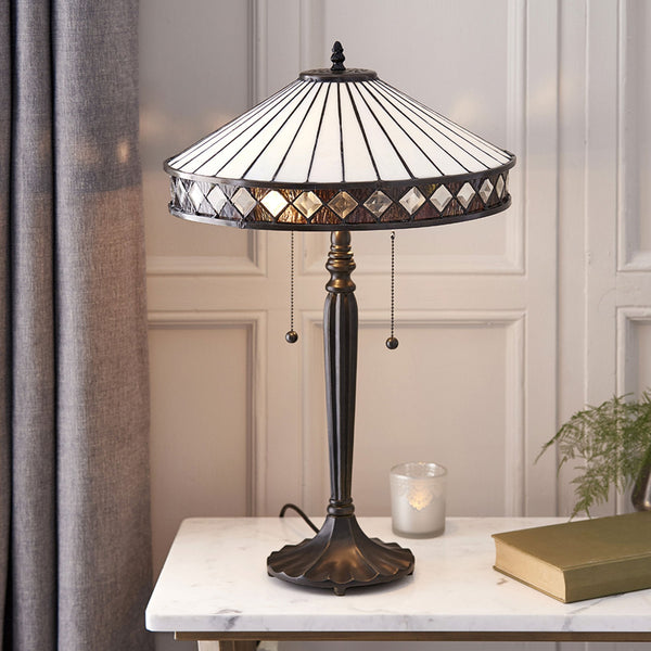Table lamp with a patterned white shade and dark base, resting on a white table.