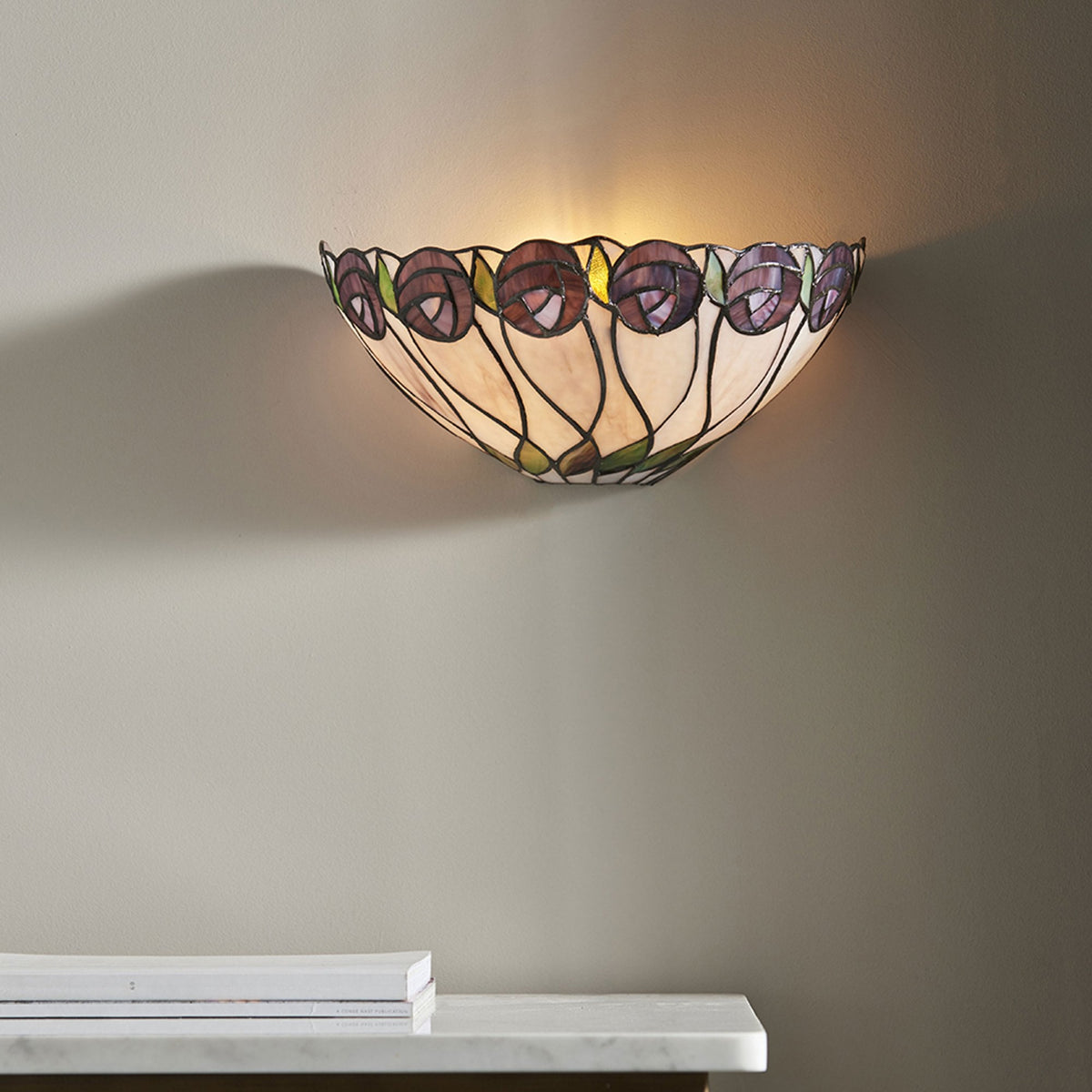 A Tiffany wall light with a purple stained glass flower design mounted above a white shelf.