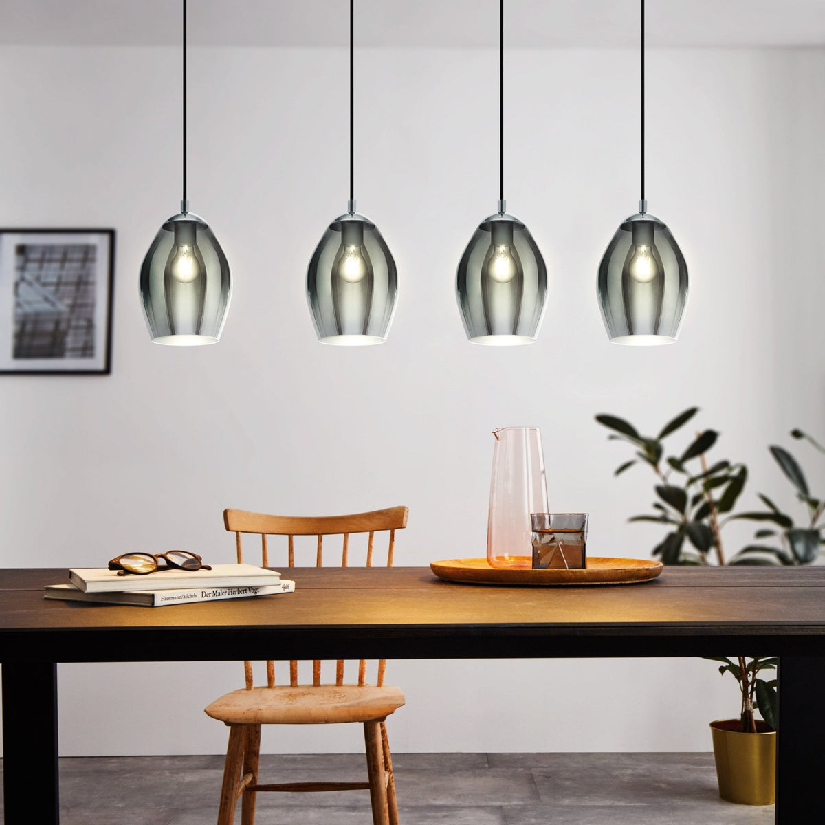 Four grey glass pendant lights hang above a dark wooden dining table with books, glasses, and a plant.