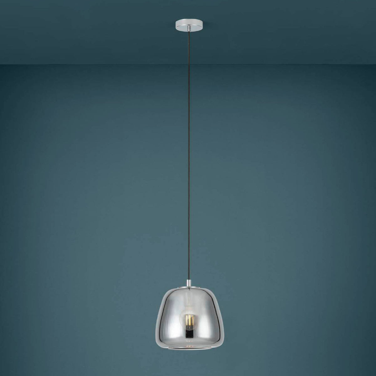 A sleek chrome pendant light hangs against a teal wall, showcasing its reflective finish.