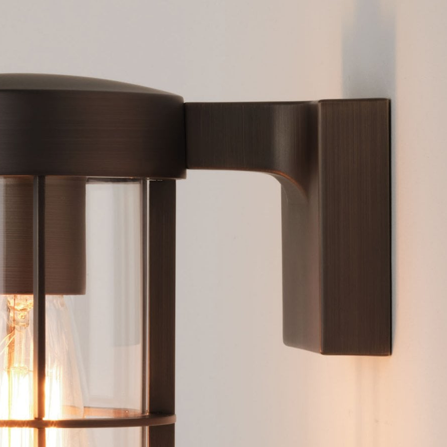 Close up of a bronze outdoor wall light with a clear glass shade and exposed filament bulb