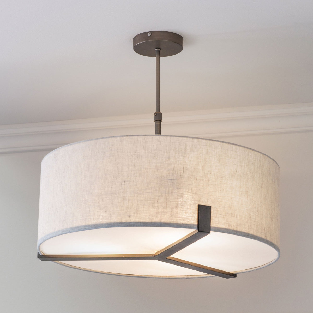 A large, round pendant light with a light-colored fabric shade and dark metal accents hanging from a ceiling.