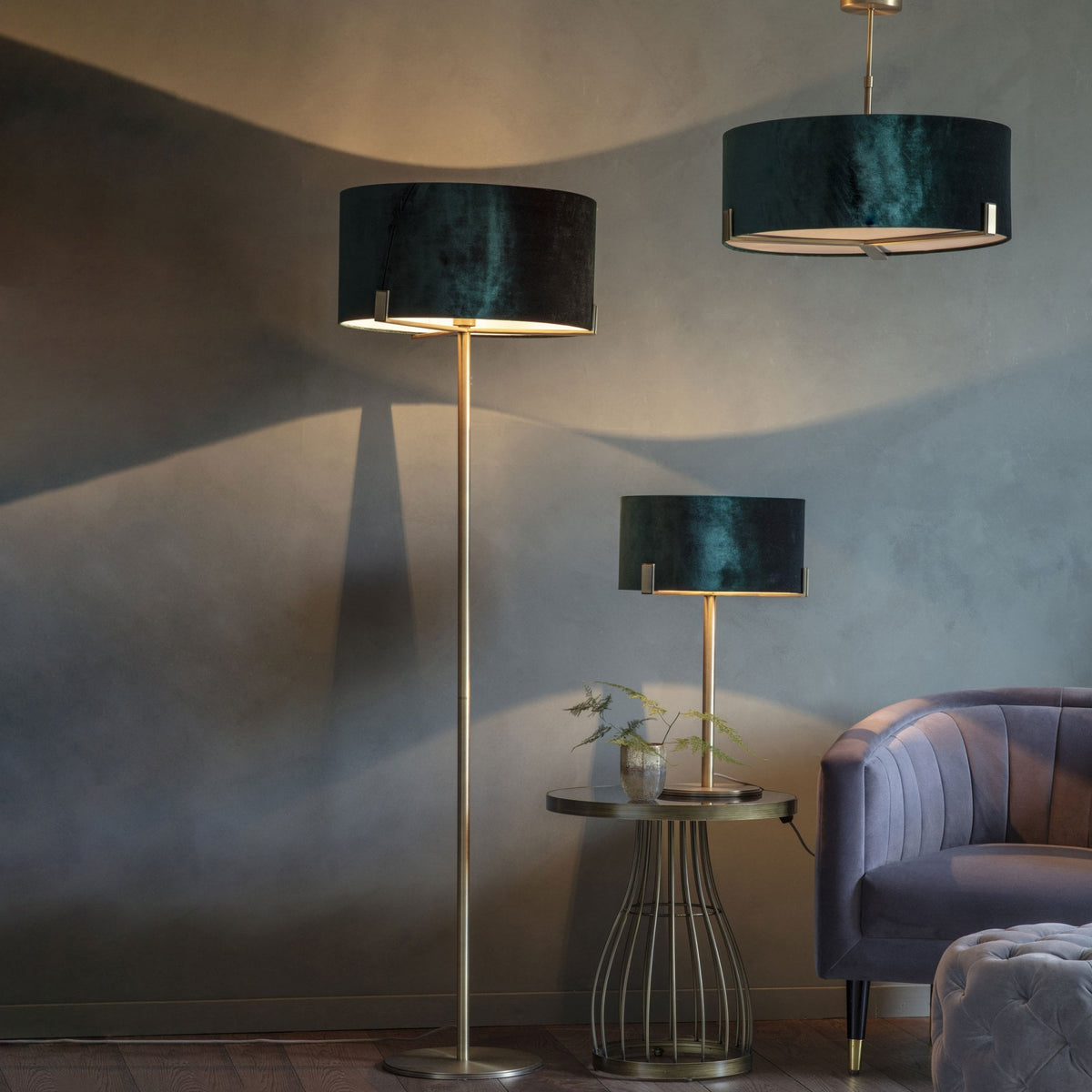 A living room with a dark green velvet drum pendant, floor lamp, and table lamp, alongside a purple sofa.