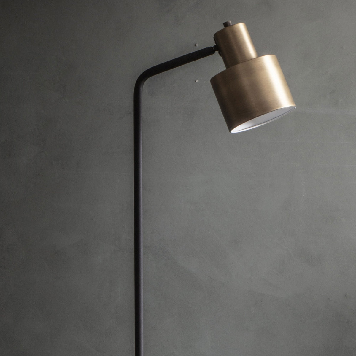 Close-up of a brass and black metal floor lamp with a lit shade against a dark wall.