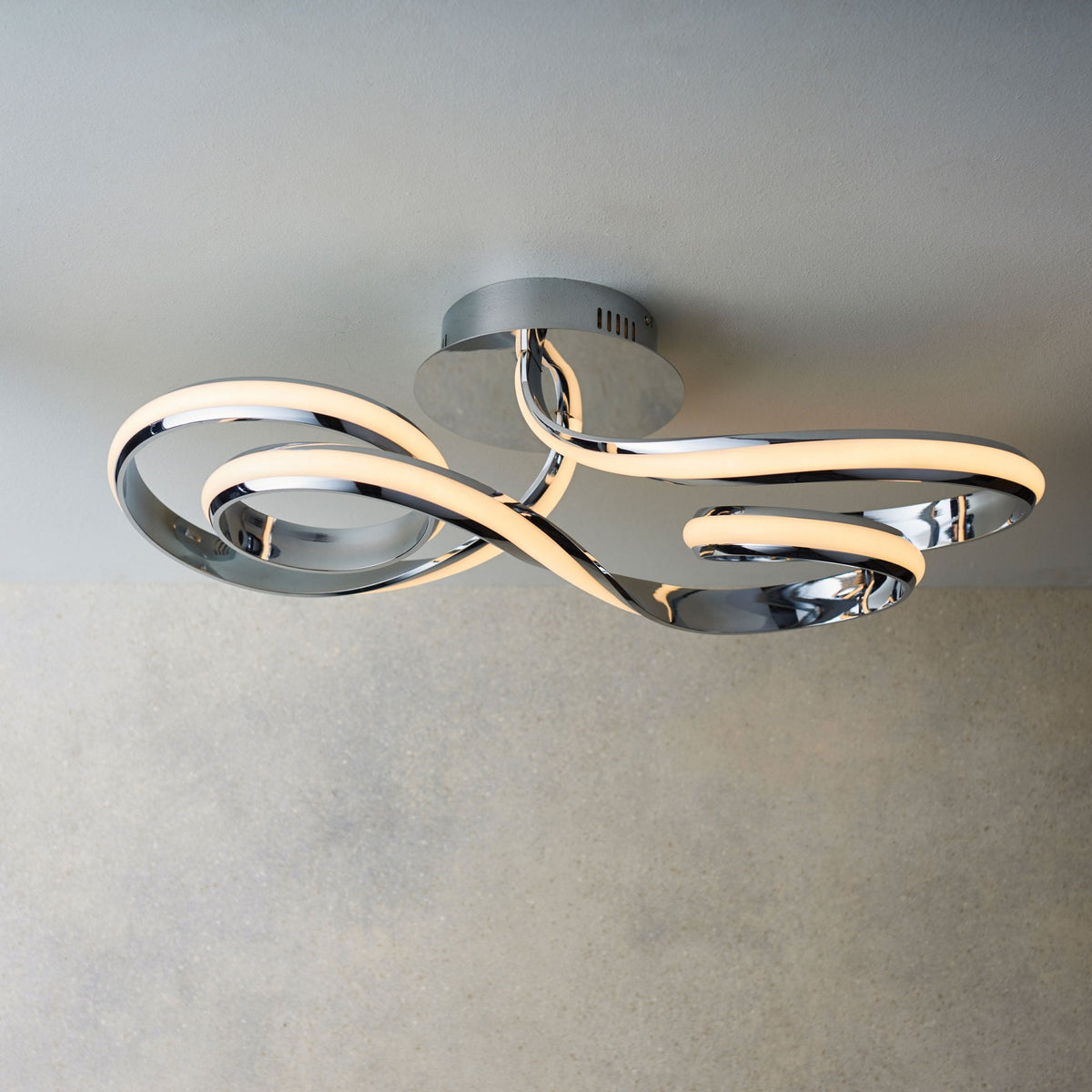 Modern chrome ceiling light with three intertwined, illuminated LED strips forming an abstract design.