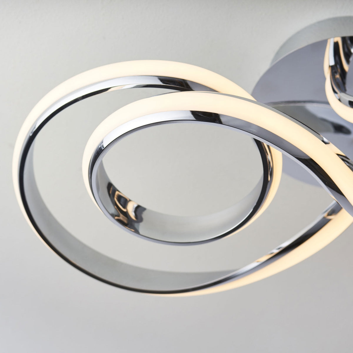 Close-up of a modern chrome ceiling light, showing the illuminated LED strip curving in a spiral.