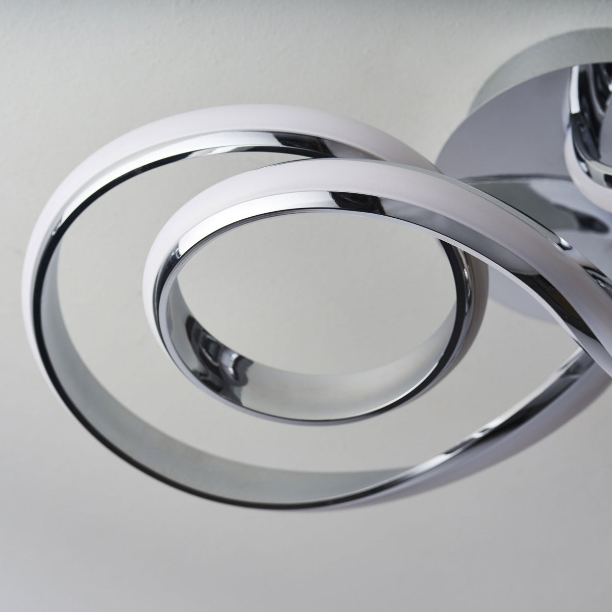 Close-up of a modern chrome ceiling light, showing the unlit LED strip curving in a spiral.
