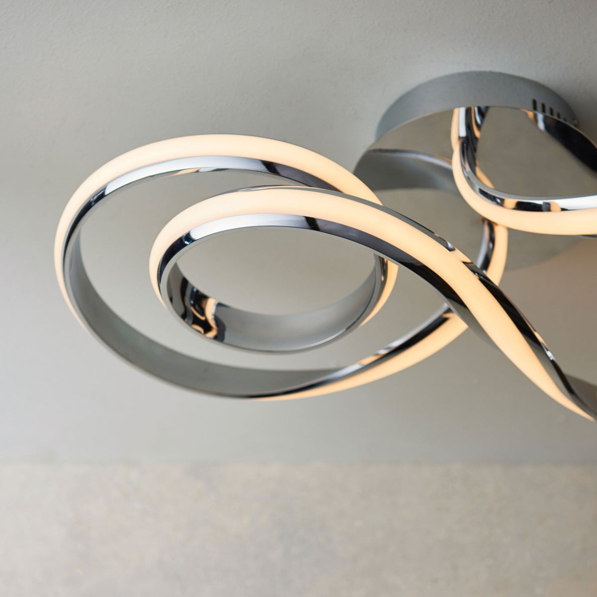 Close-up of a modern chrome ceiling light, showing the illuminated LED strip curving in a spiral.