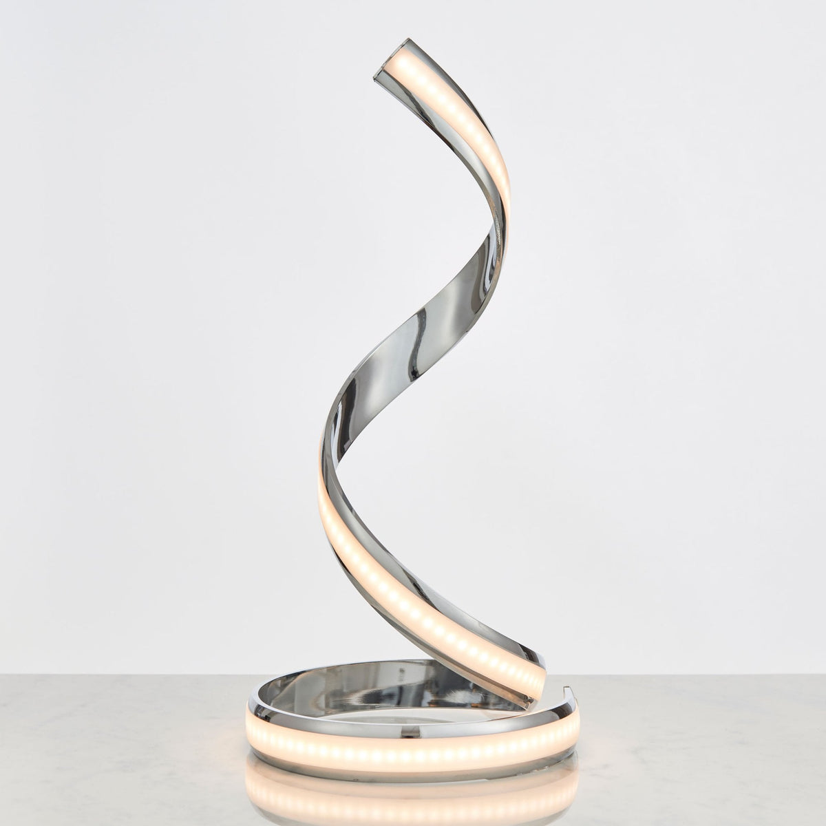 Chrome spiral LED table lamp with a glowing base and a bright, warm light strip winding up the spiral.