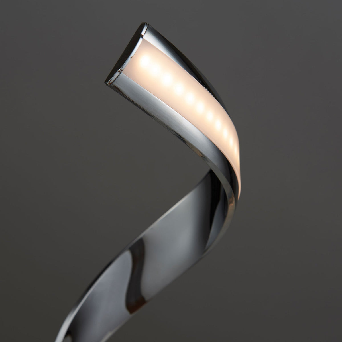 Close-up of the top of a chrome spiral LED table lamp, showing the illuminated warm light strip.