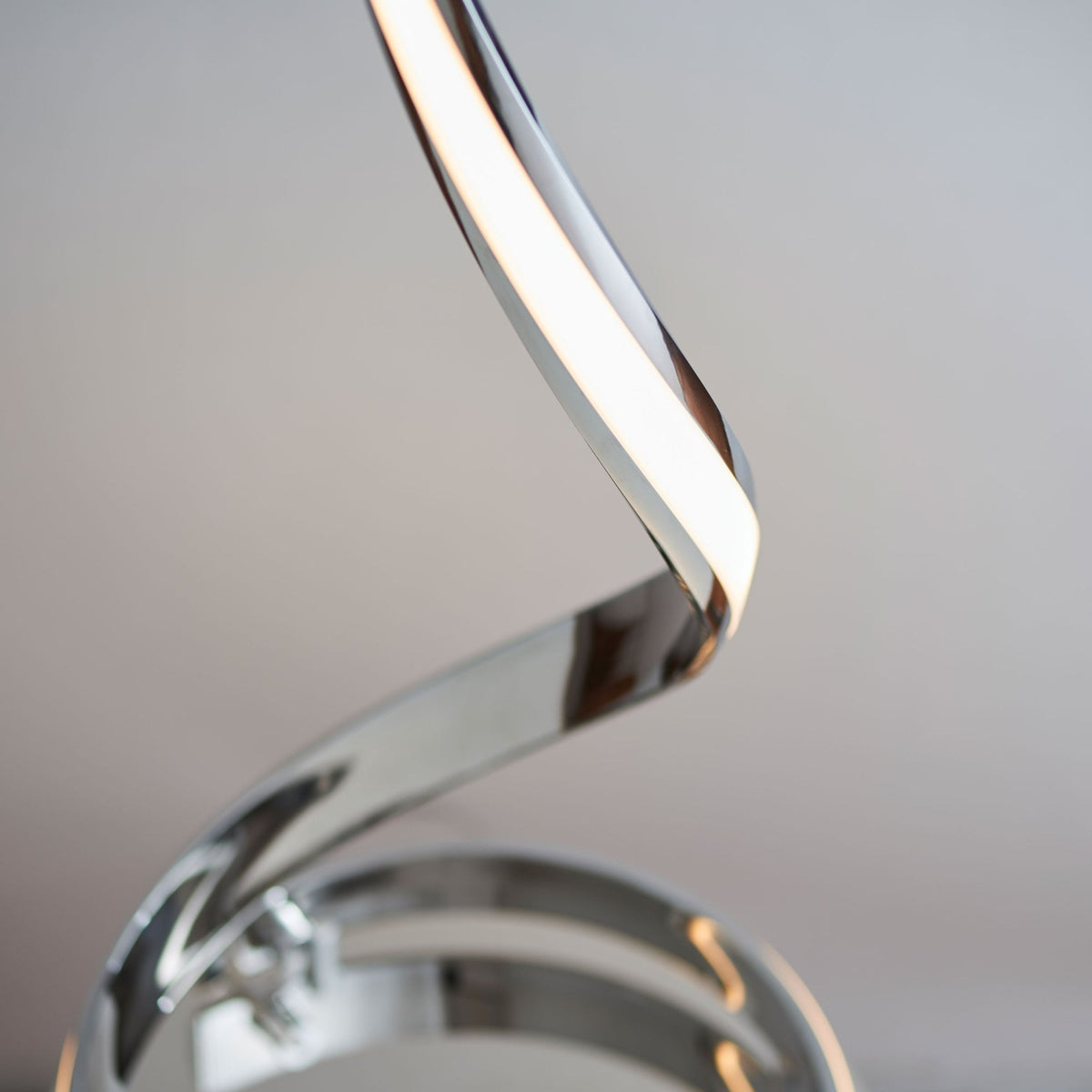 Close-up of the top of a chrome spiral LED floor lamp with a bright light strip.
