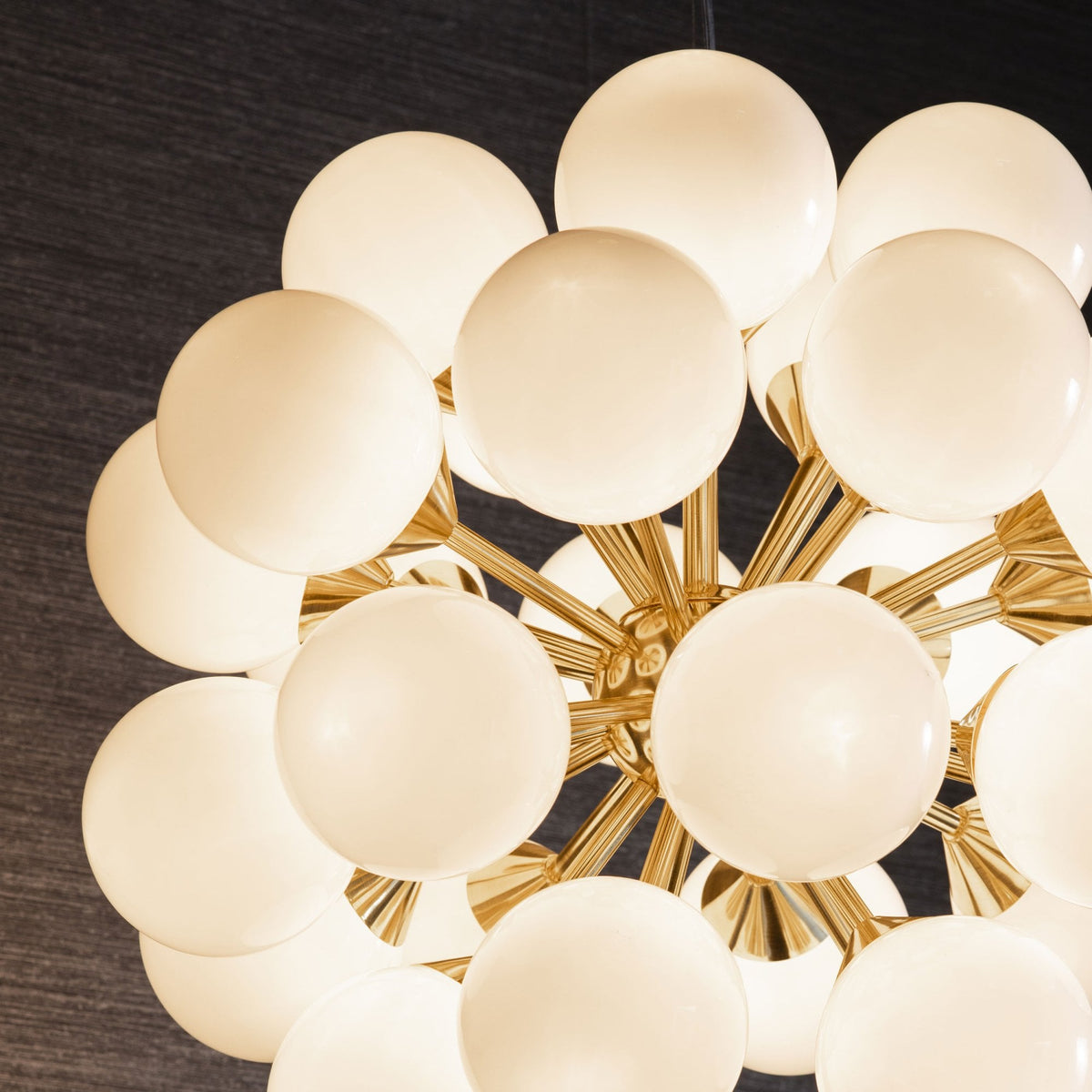 Close-up of a large, modern chandelier with many white spherical lights and a gold frame, against a dark background.