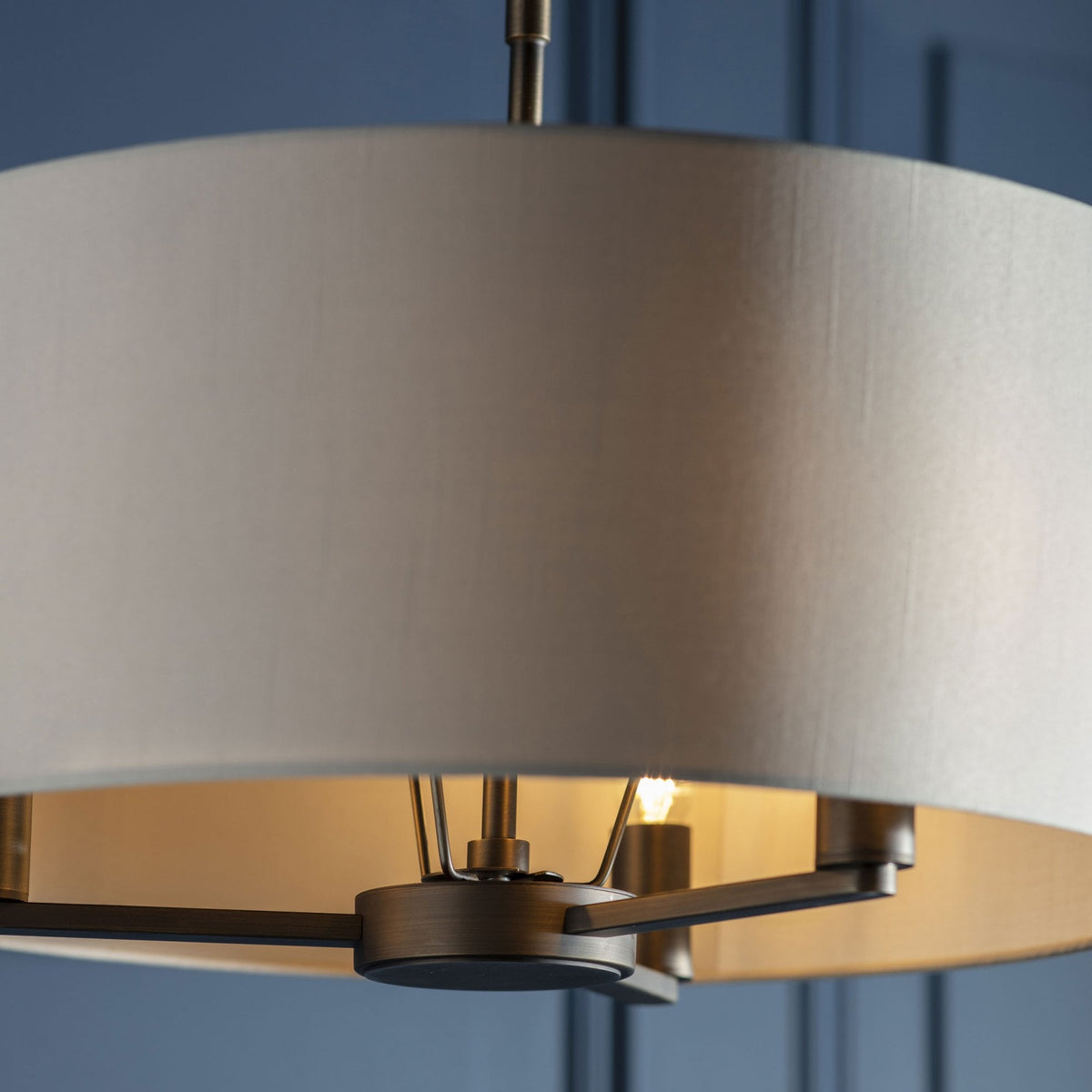 Drum pendant light with a white shade and dark bronze frame, illuminated against a blue wall.
