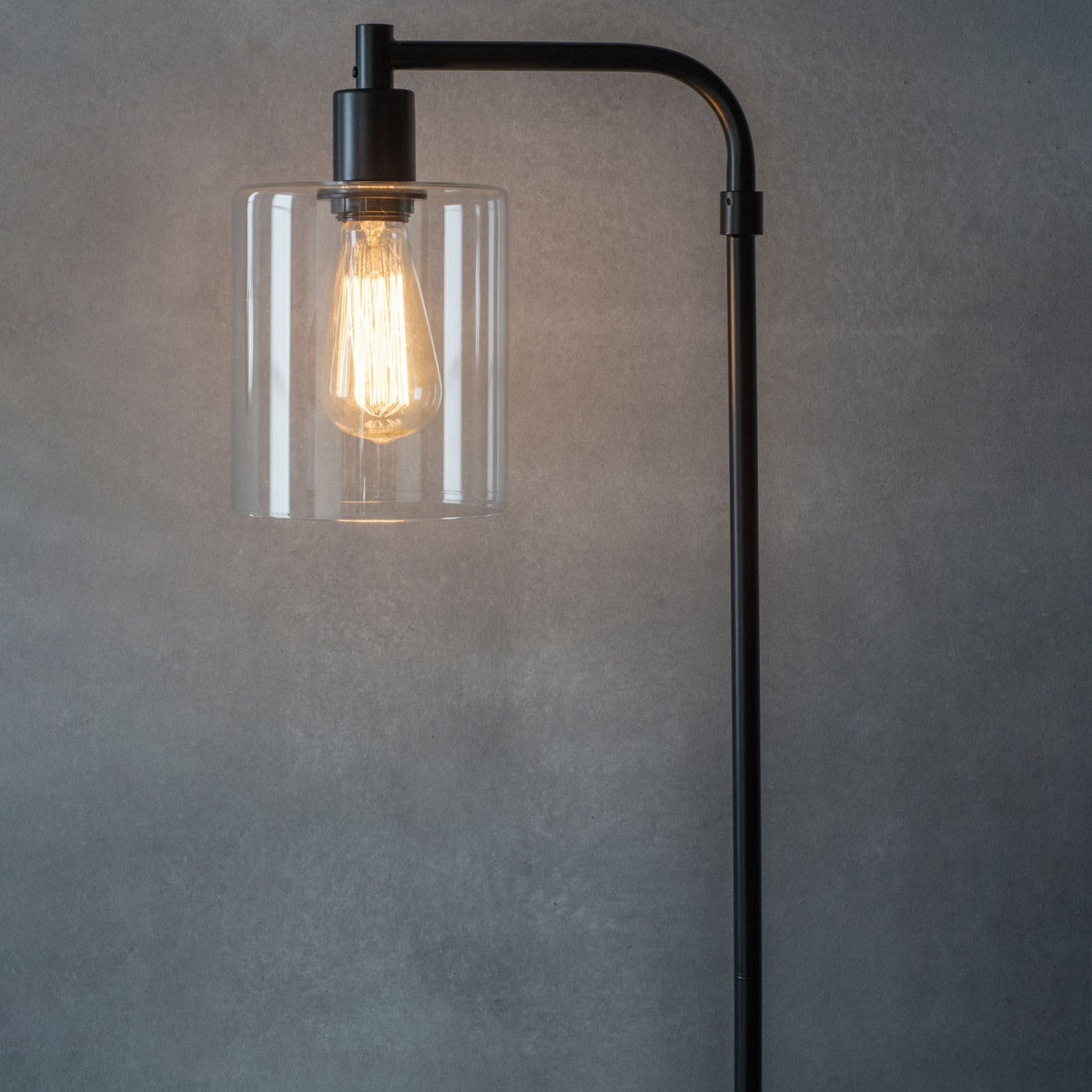Close-up of a black metal floor lamp with a clear glass shade and an exposed Edison bulb.