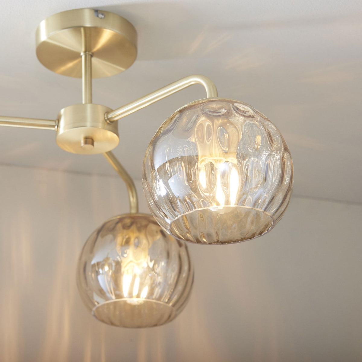 Close-up of a three-light ceiling fitting with clear glass shades and a brass finish.
