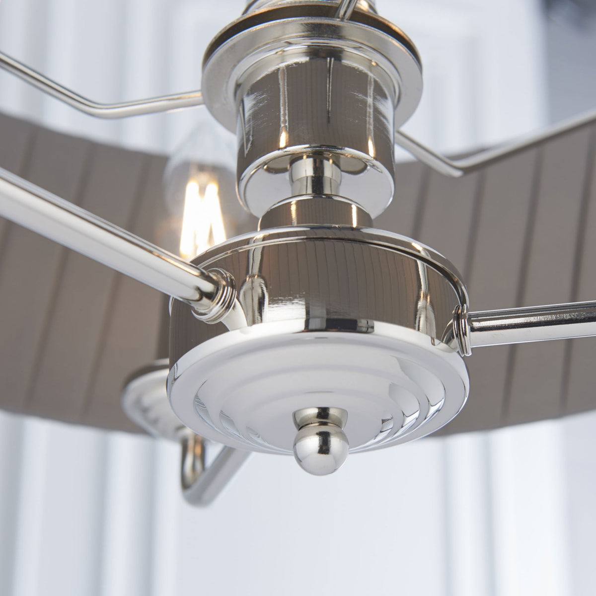 Close-up of the polished nickel hardware and exposed bulb of a chandelier.