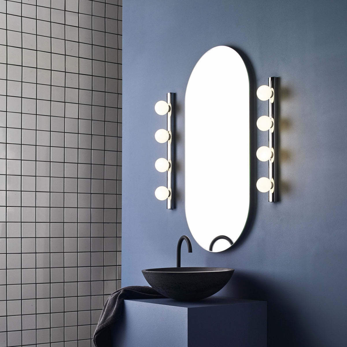 Oval mirror with vertical lights on each side above a black sink and faucet.