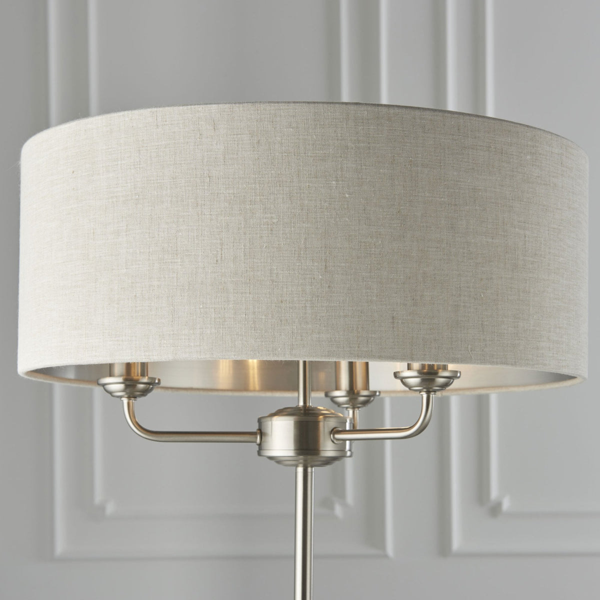 Close-up of the light fabric shade and brushed nickel base of a floor lamp, showing three bulbs.