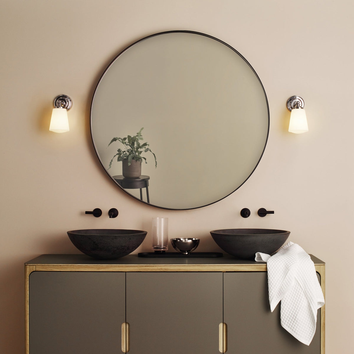 Bathroom vanity with two black vessel sinks, a round mirror, and two wall sconces