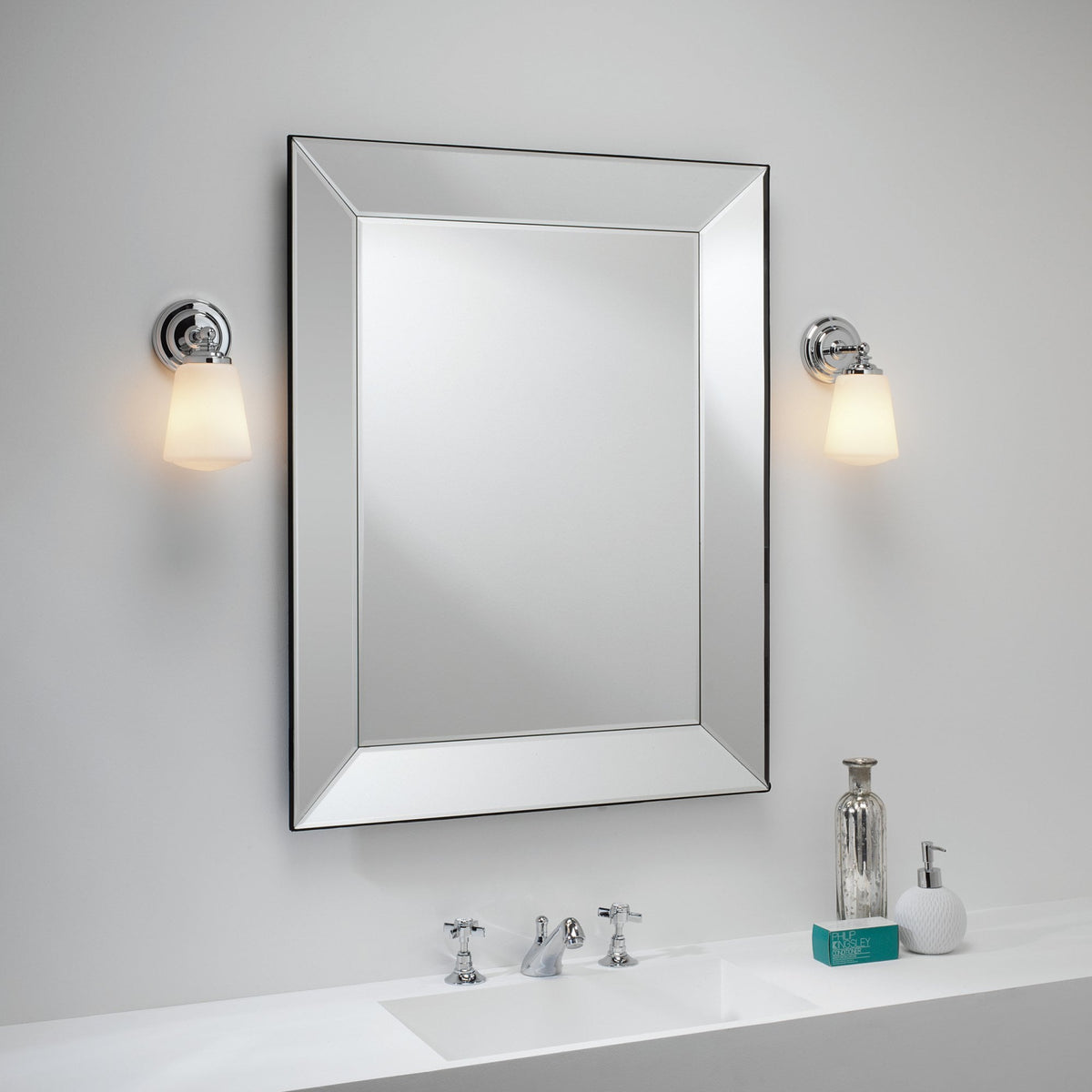 Rectangular mirror with a beveled frame, two wall sconces, and a white sink with chrome fixtures