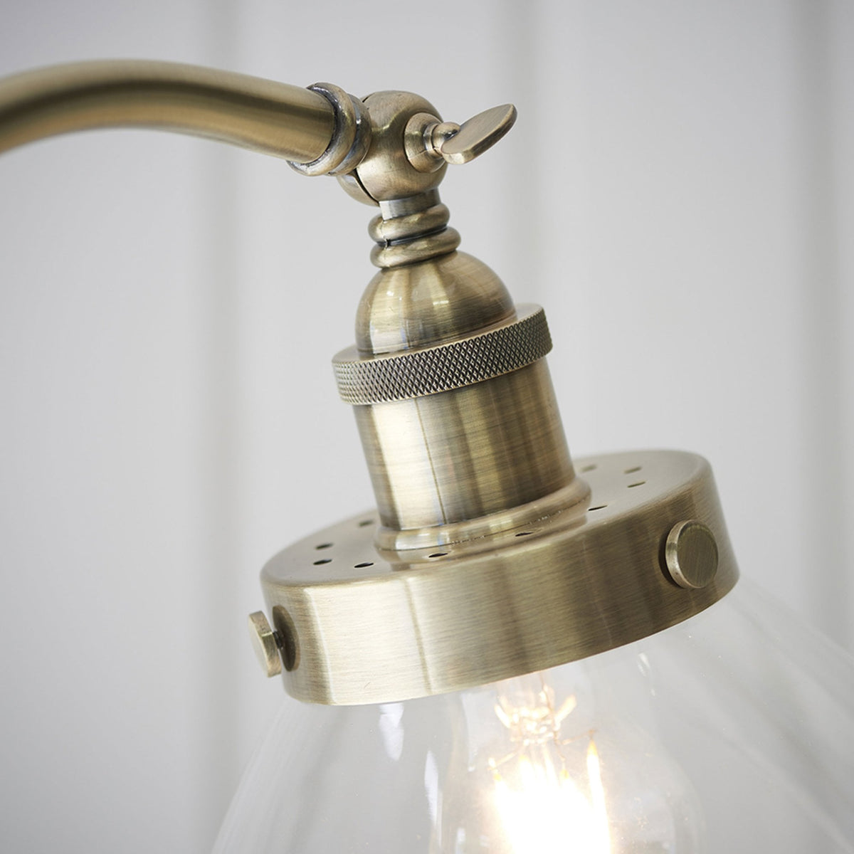 Close-up of the antique brass fitting and clear glass shade of a floor lamp, with a visible lightbulb.
