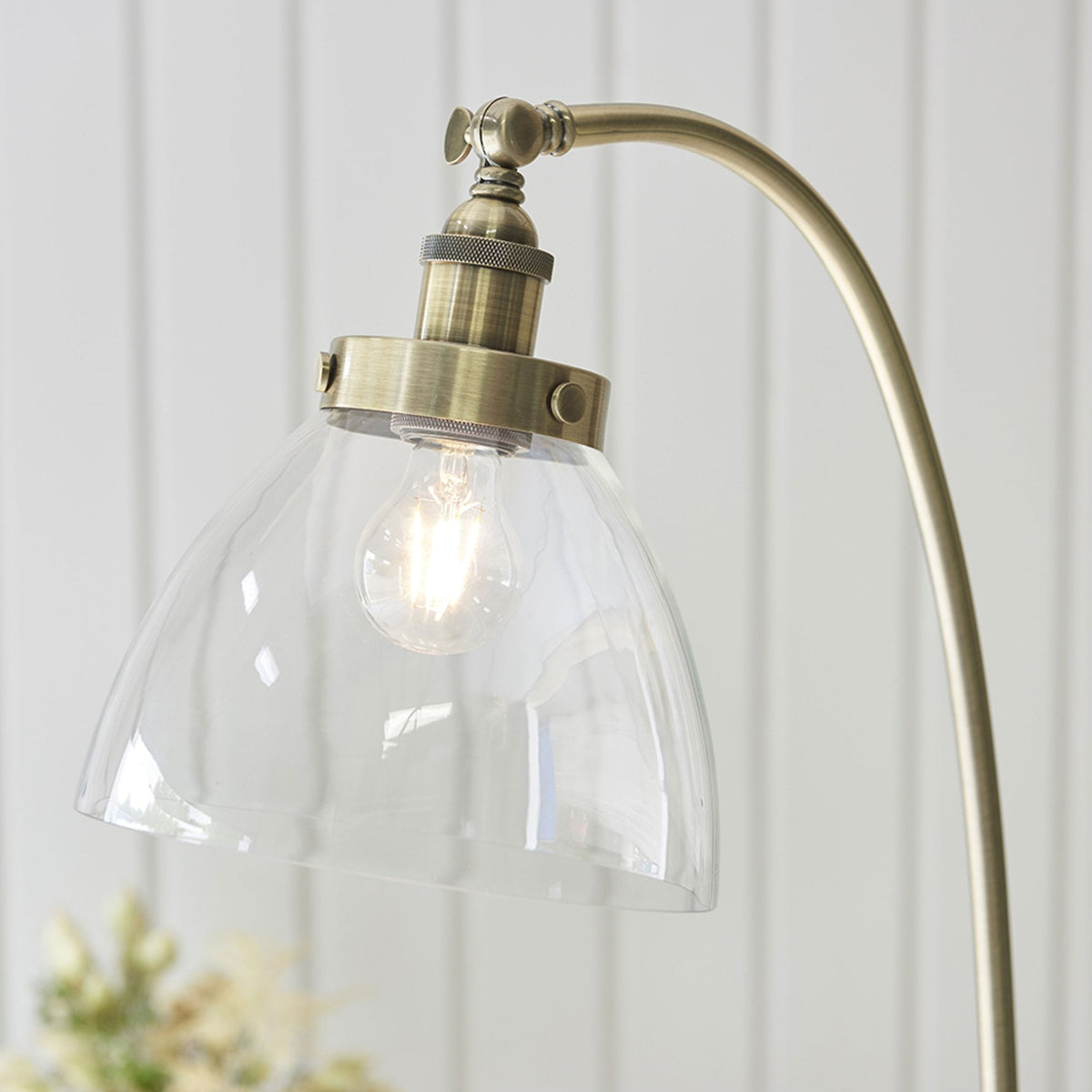 Close-up of the clear, fluted glass shade and antique brass fitting of a floor lamp, with the bulb glowing.