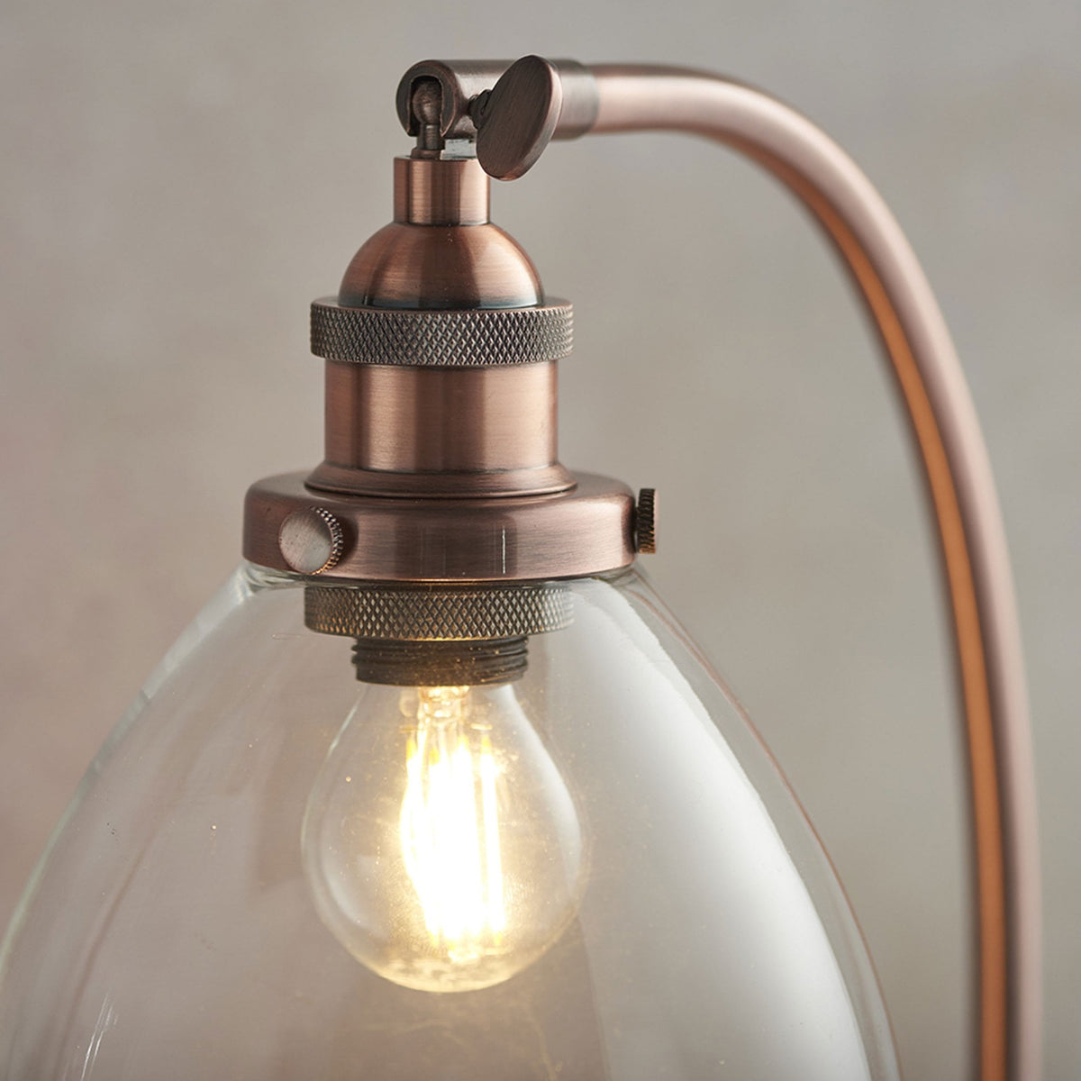 Close-up of the copper fitting and clear glass shade of a table lamp, with a visible light bulb.