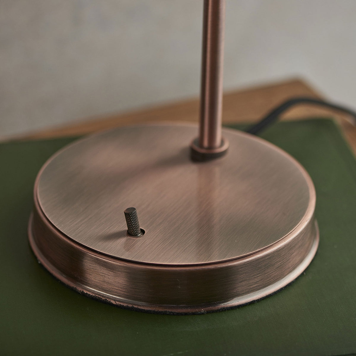 Close-up of the round, brushed copper base of a table lamp with a small toggle switch.