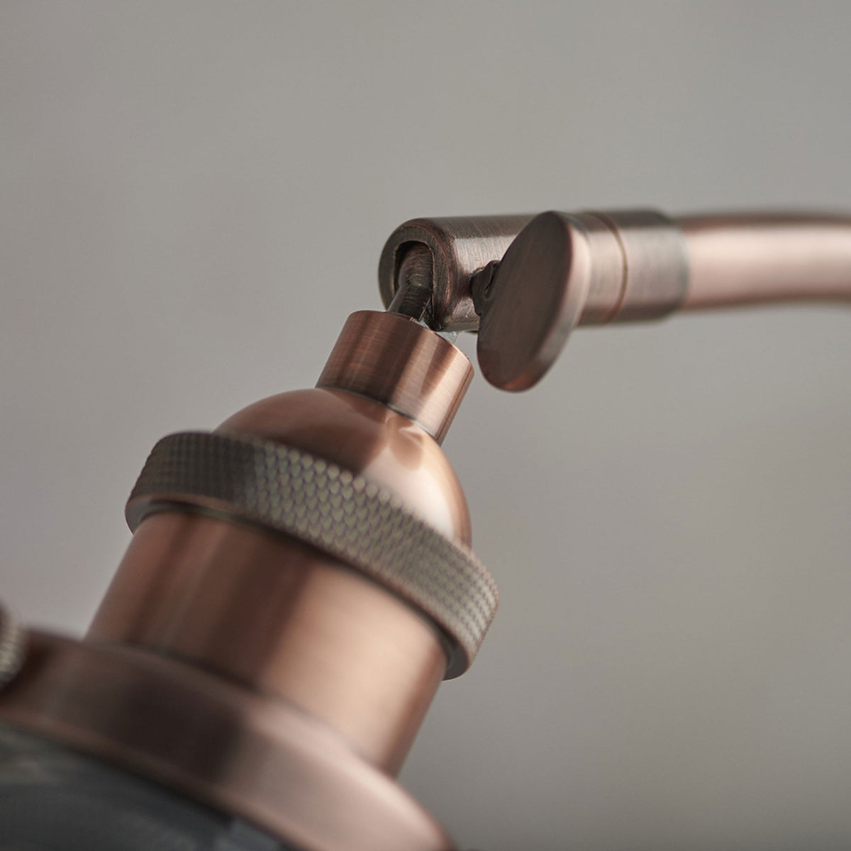 Close-up of the adjustable joint and copper fitting connecting the curved arm to the clear glass shade.