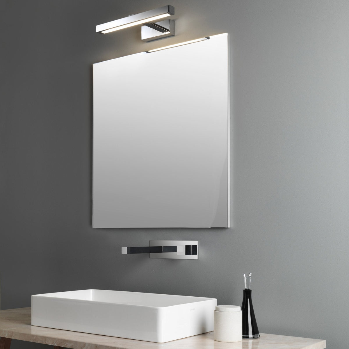 Rectangular mirror with a chrome light fixture above and a wall-mounted faucet over a white sink