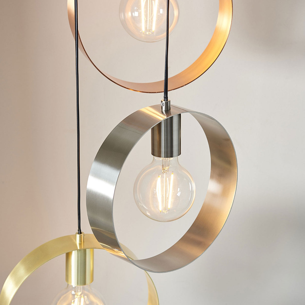 Close-up of three pendant lights with circular metal shades in copper, silver, and gold, illuminating a room.