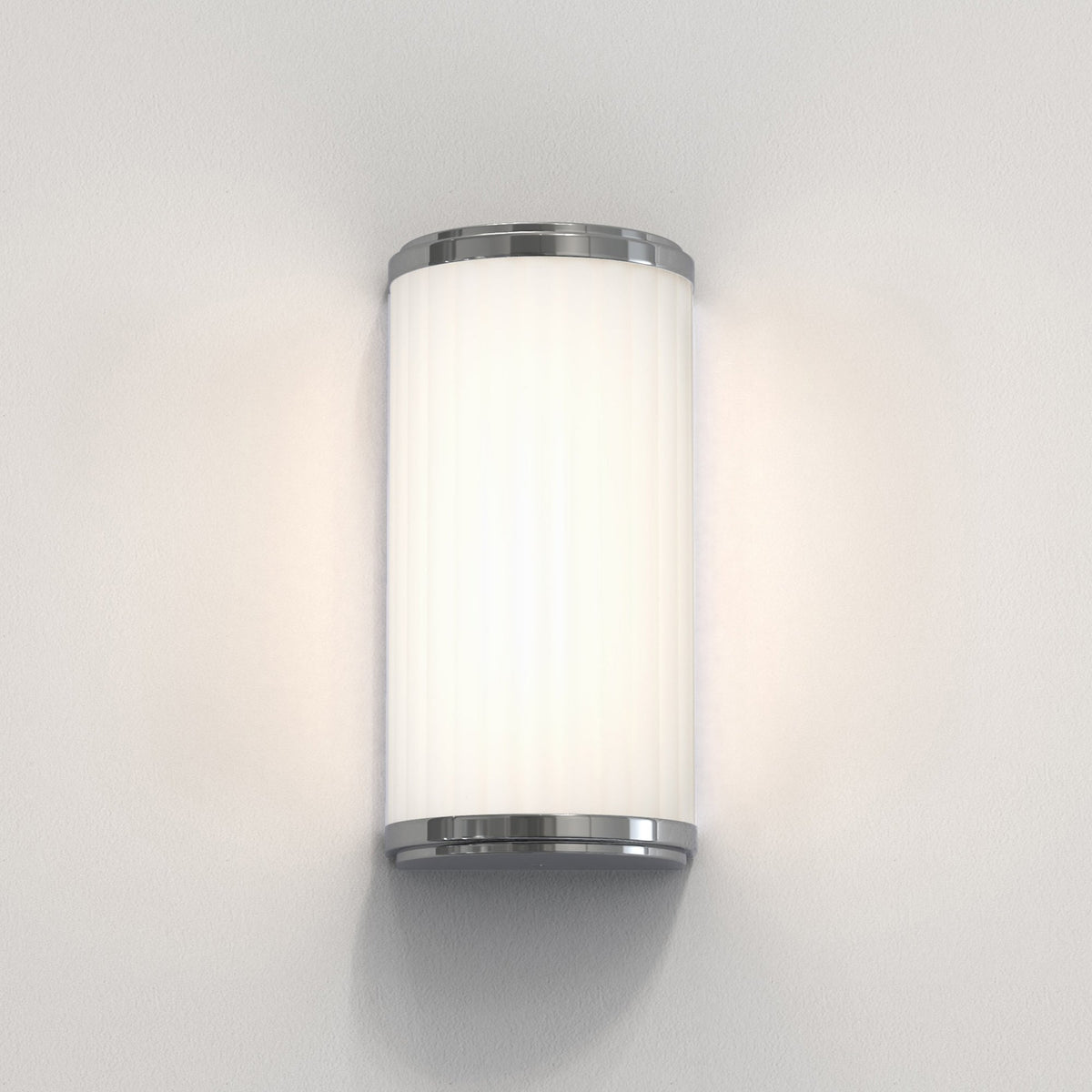 Cylindrical wall sconce with a white ribbed shade and polished chrome accents, emitting a warm glow