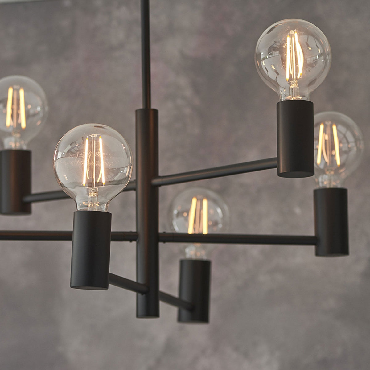 Close-up of a black chandelier with six exposed bulbs against a dark gray wall.